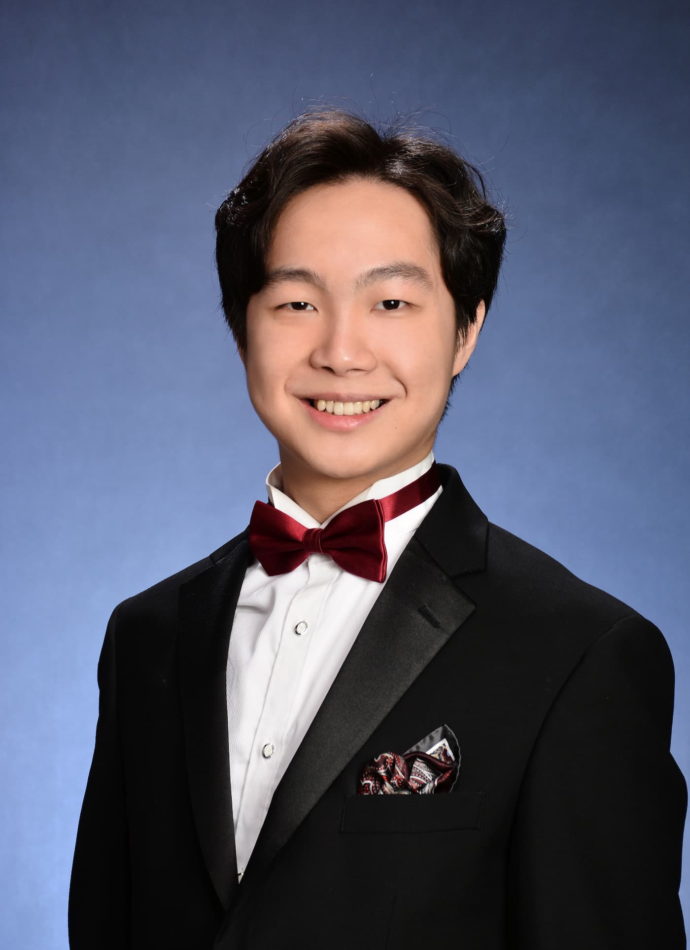 Henry Cao's professional headshot Henry Cao's smiles in a tux with a red tie in his professional headshot