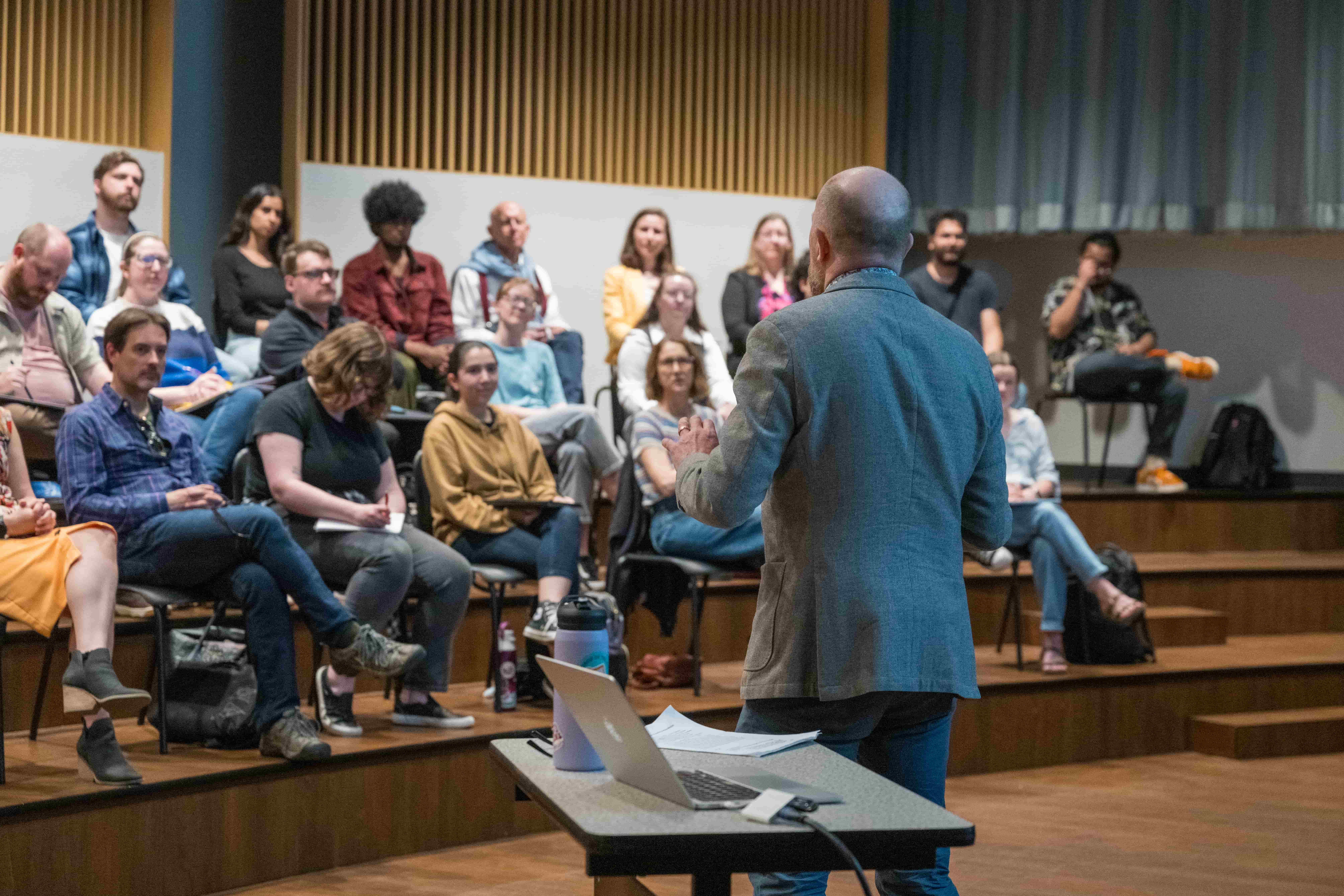 Photo of a lecture with a professor teaching to a group of seated students and faculty in a lecture room