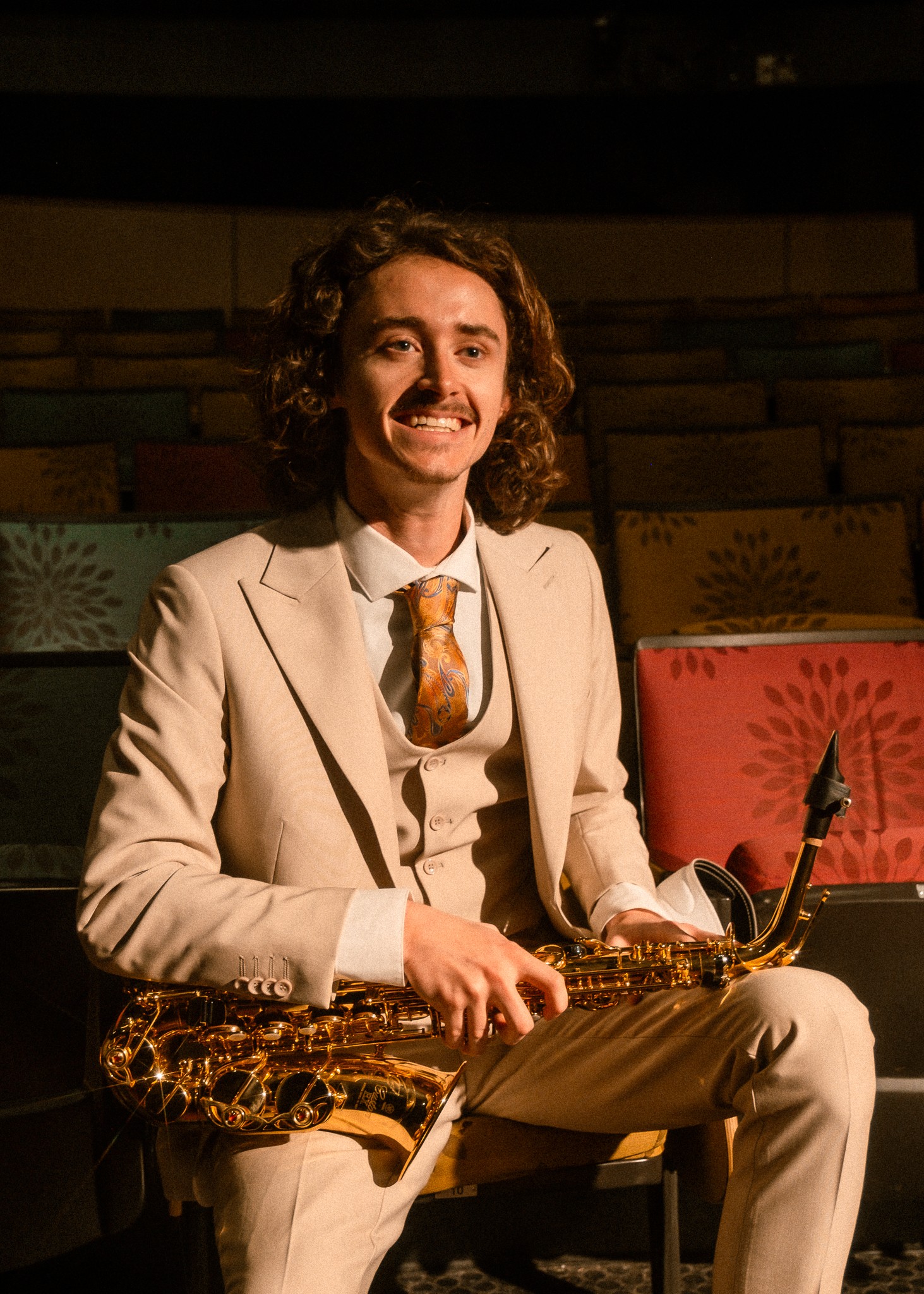Cameron Montgomery headshot Cameron Montgomery, dressed in a tan suit, holds an alto saxophone in his professional headshot