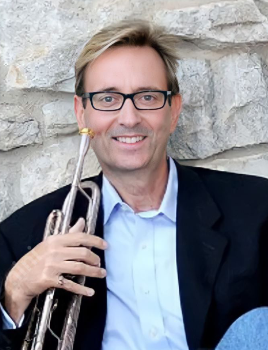 David B. Hooten with trumpet in front of stone wall. 