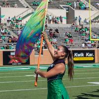 A color guard member holds a vibrant, multicolored flag up at the 45