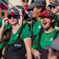 Two band members in green T-shirts and black bib pants watch the football game