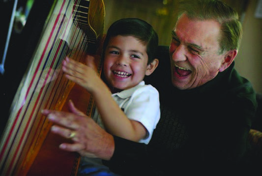 Ortiz with an elementary student playing a harp.  They both have big smiles