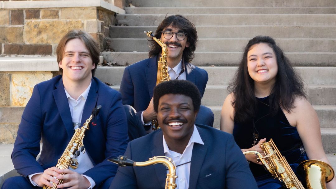 Myriad Saxophone Quartet members sit on concrete steps holding their instruments.